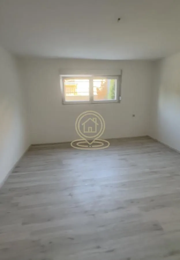 Prazna svetla soba sa prozorom i laminatom na podu.