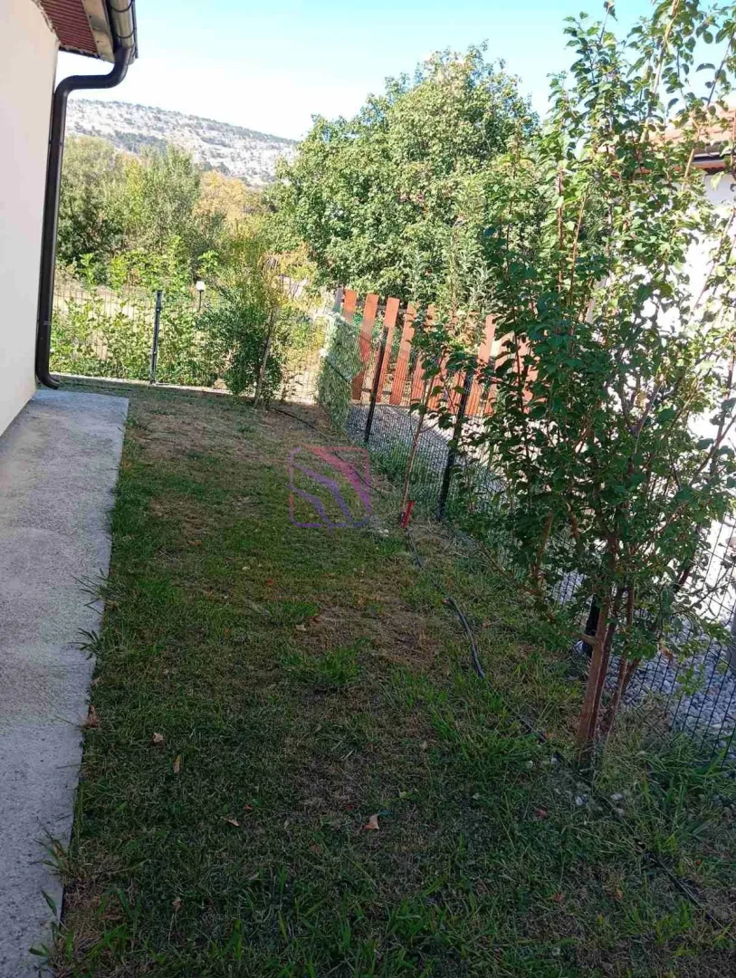 Small grassy yard with a fence and greenery next to the house.