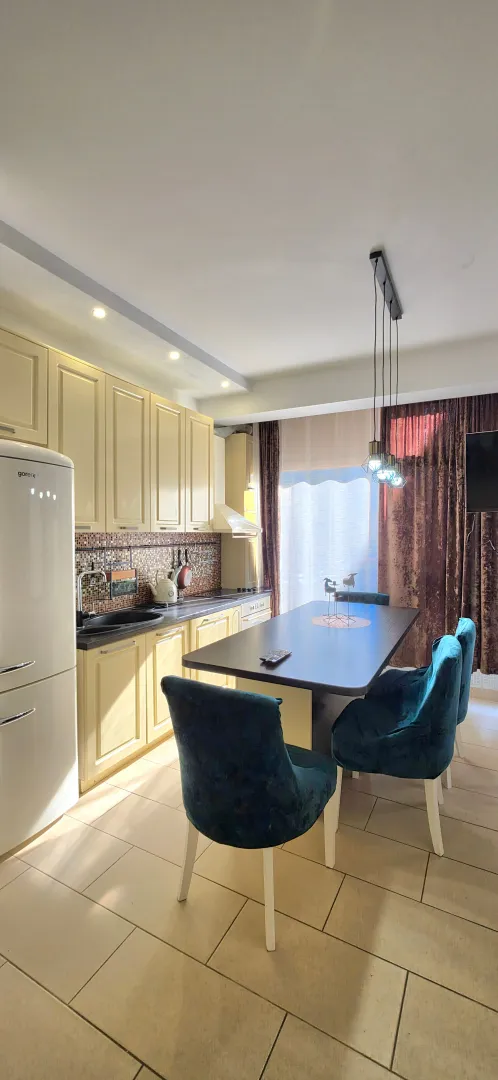 Kitchen with dining area equipped with beige cabinets and a dark dining table with blue chairs.