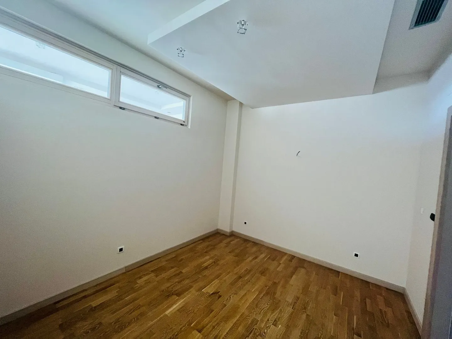 An empty room with parquet flooring and bright walls.