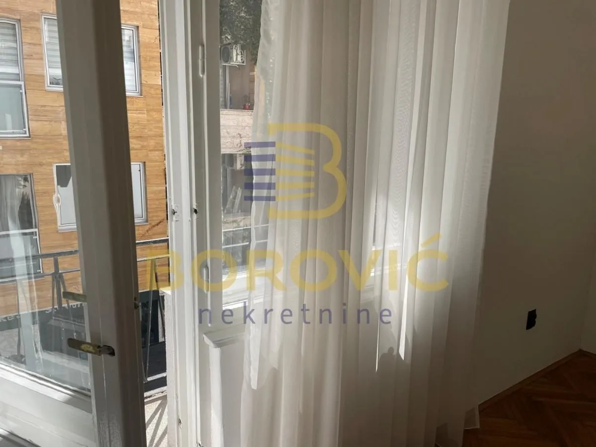 View through the window with white curtains overlooking surrounding buildings and the street.