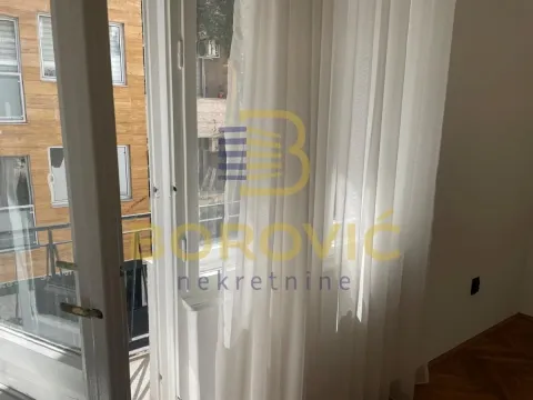 View through the window with white curtains overlooking surrounding buildings and the street. - image 8