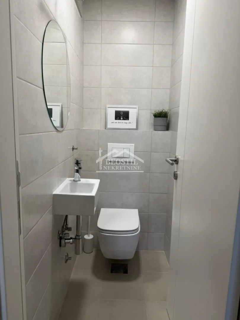 Manje kupatilo obloženo svetlim pločicama sa ugradnim toaletom i umivaonikom.