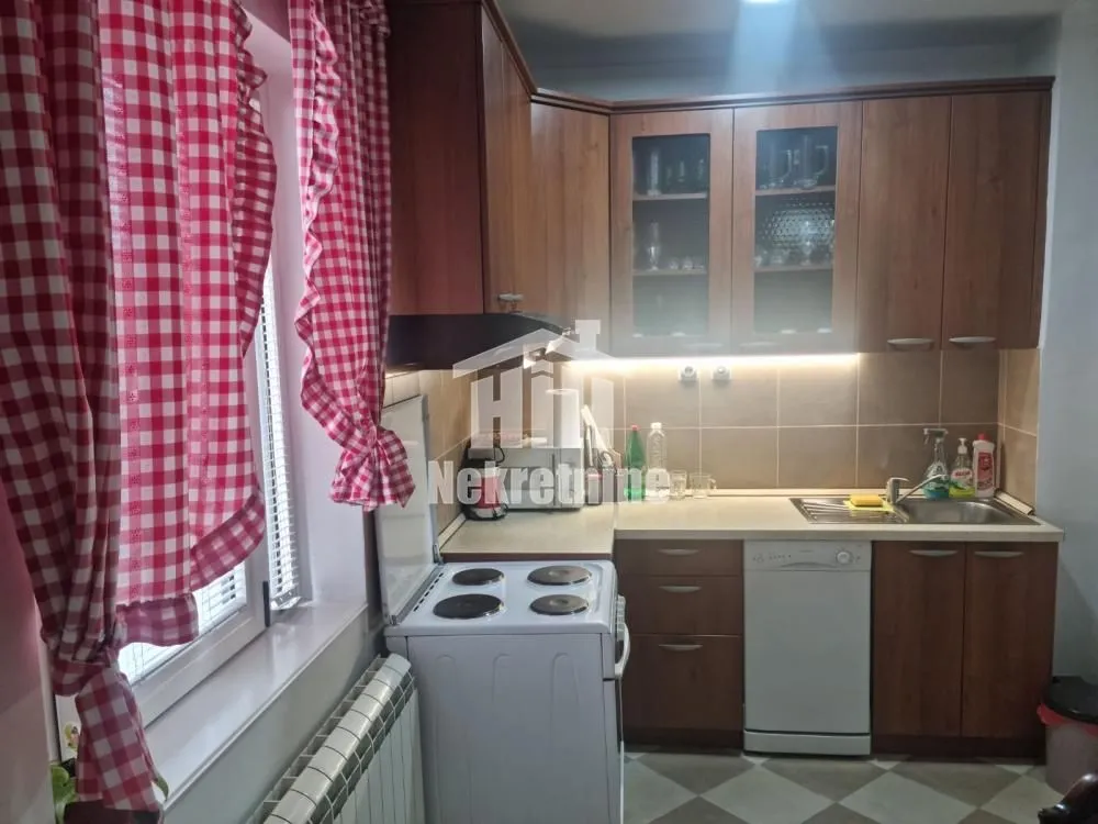 Kuhinja sa drvenim elementima, šporetom i prozorom sa kariranim zavesama.