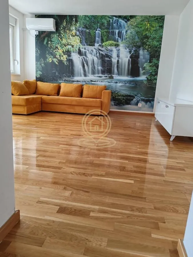 Dnevna soba sa žutom garniturom i tapetom sa motivom vodopada.