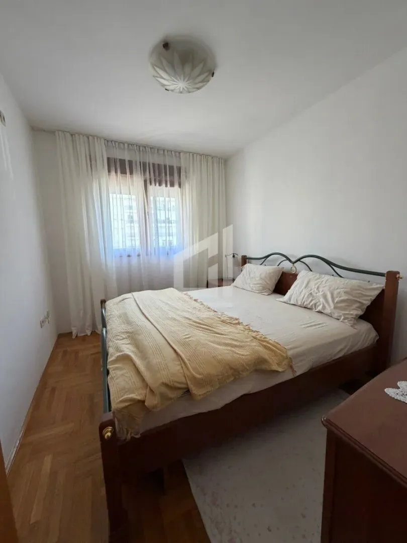 Spavaća soba sa bračnim krevetom i prozorom prekrivenim bijelim zavjesama.