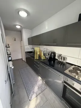Dugačka kuhinja sa tamnim elementima i ugrađenim aparatima. - image 5