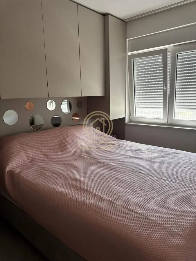 Nameštena spavaća soba sa bračnim krevetom, ugradnim ormarima i ukrasnim ogledalima na zidu.