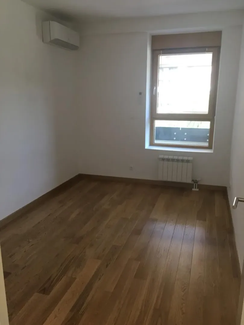 Empty room with wooden flooring, an air conditioning unit, and a window.