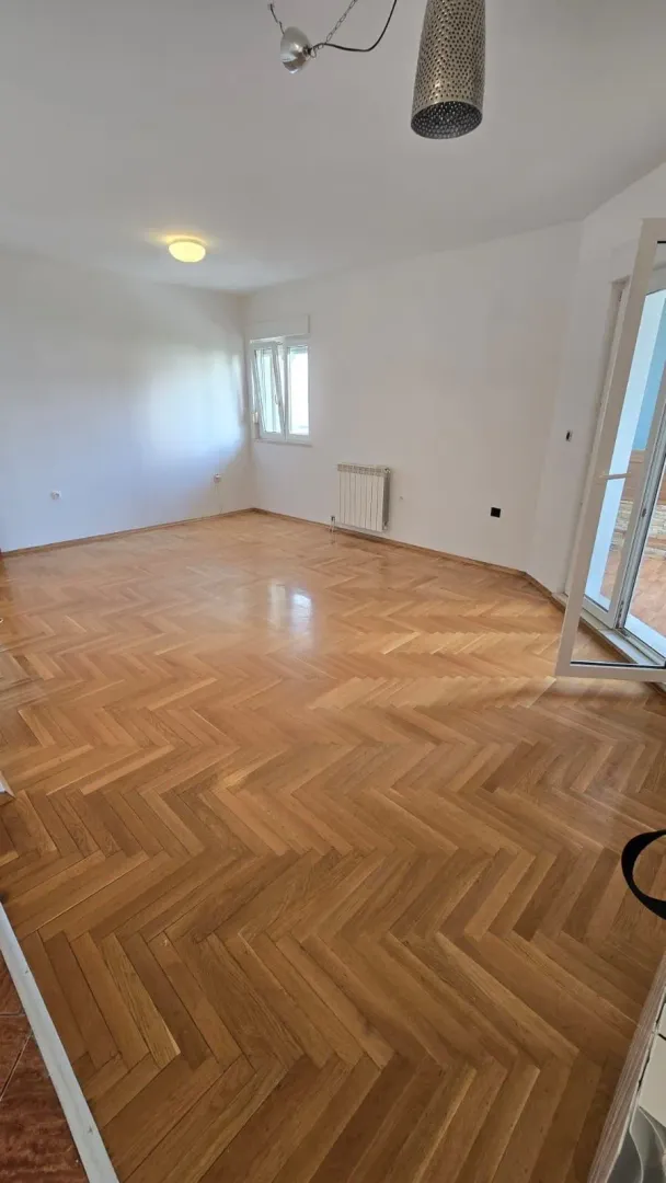 Prazna soba sa parketom i bijelim zidovima.