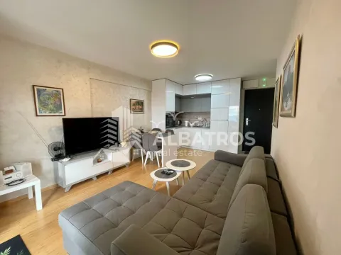 Living room with a sofa, TV, and kitchen in the background. - image 2