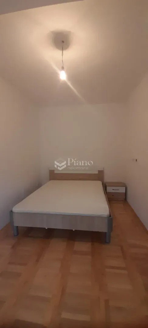 Manja spavaća soba sa bračnim krevetom i drvenim podom.