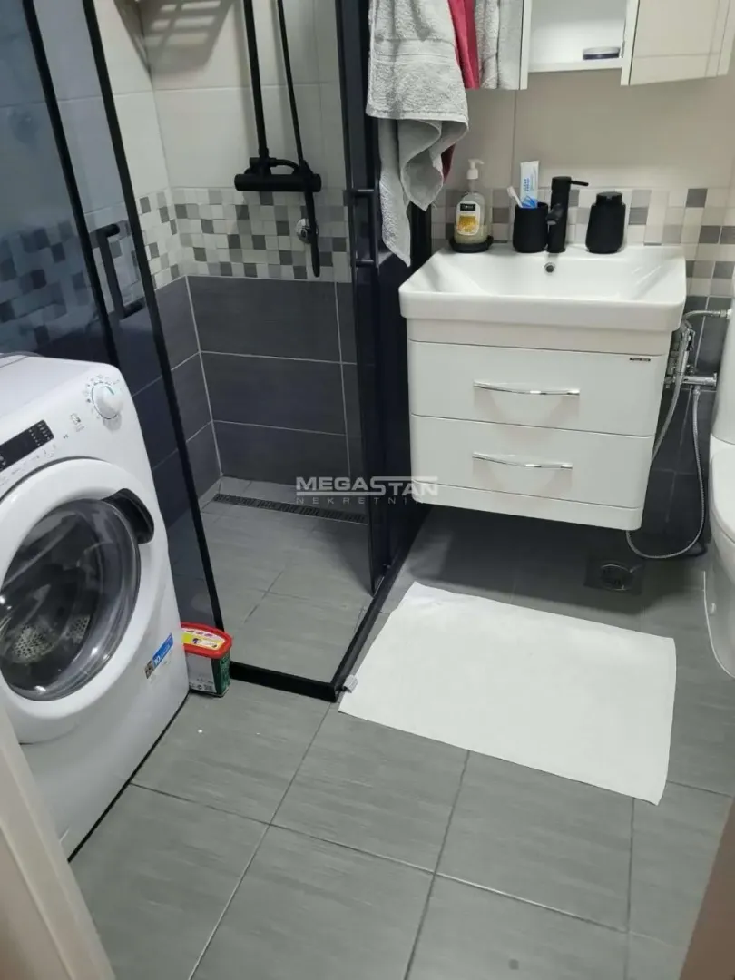 Moderno opremljeno kupatilo sa tuš kabinom i veš mašinom.