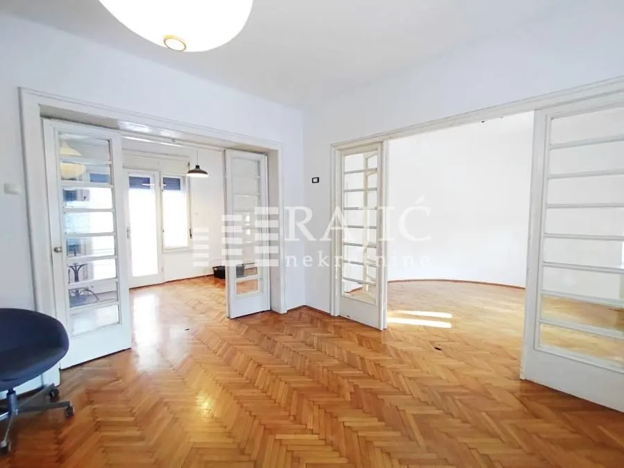 Spacious living room with hardwood parquet flooring and double glass doors.