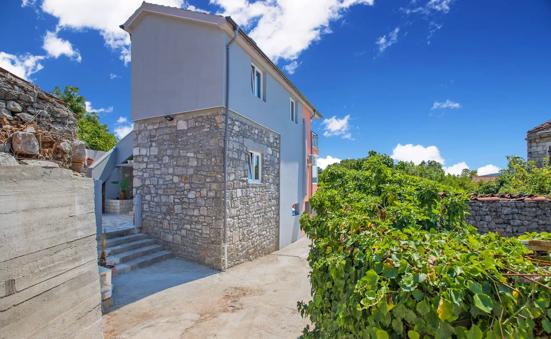 Pogled na spoljašnjost kuće sa kamenom fasadom i dvorištem.
