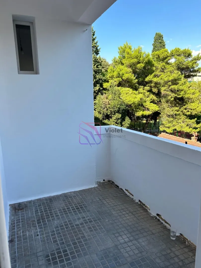 Nenamješten balkon sa pogledom na zelenilo i drveće.