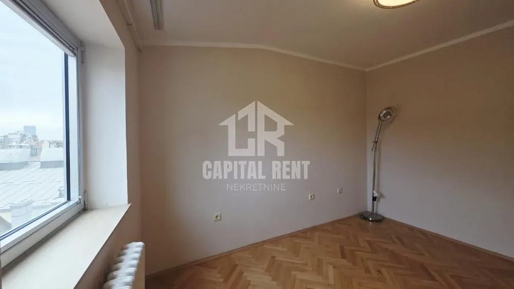 Empty room with hardwood flooring and a large window.