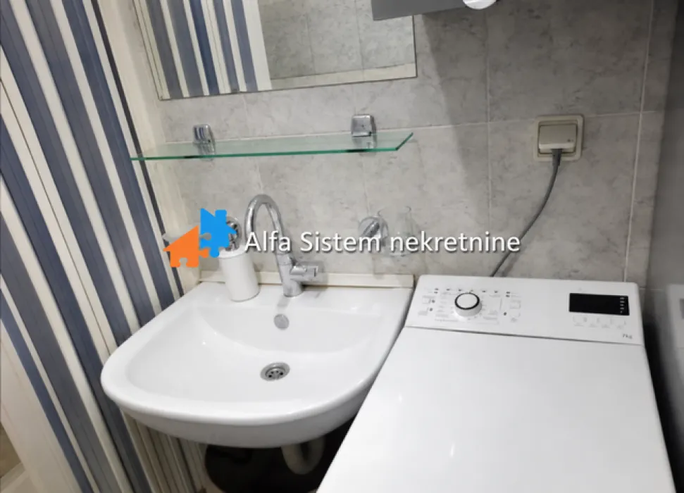 Manje kupatilo sa umivaonikom, ogledalom i mašinom za veš.