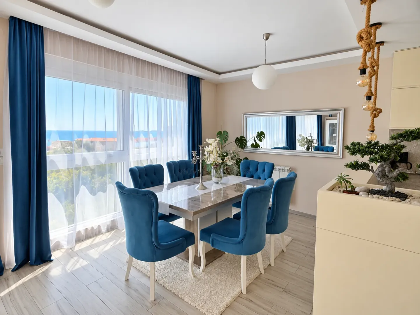 Dining area with a table and blue chairs next to a large window with a sea view.