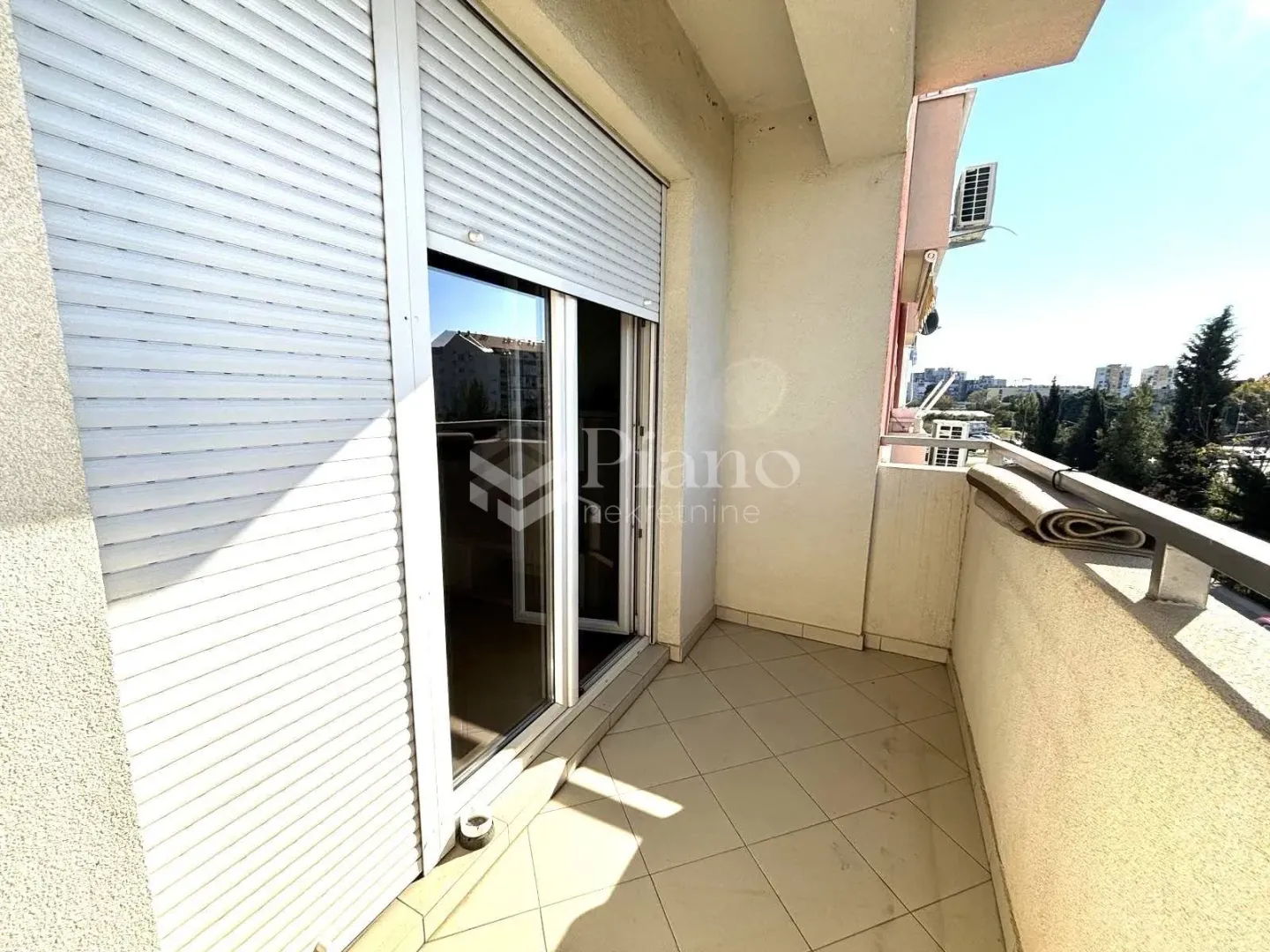 A view of a spacious balcony with ceramic tiles and window shutters.