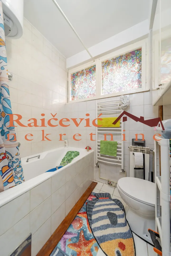 Kupatilo opremljeno kadom, wc šoljom i prozorom sa vitražom.