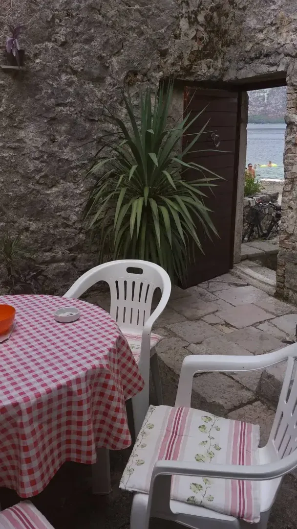 Dvorište sa kamenim zidovima i stolom sa stolicama ispred otvorenih vrata sa pogledom na more.