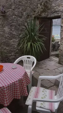 Dvorište sa kamenim zidovima i stolom sa stolicama ispred otvorenih vrata sa pogledom na more. - image 7