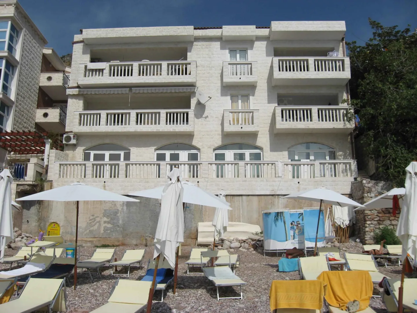 Pogled na fasadu zgrade sa plaže i ležaljkama u prvom planu.