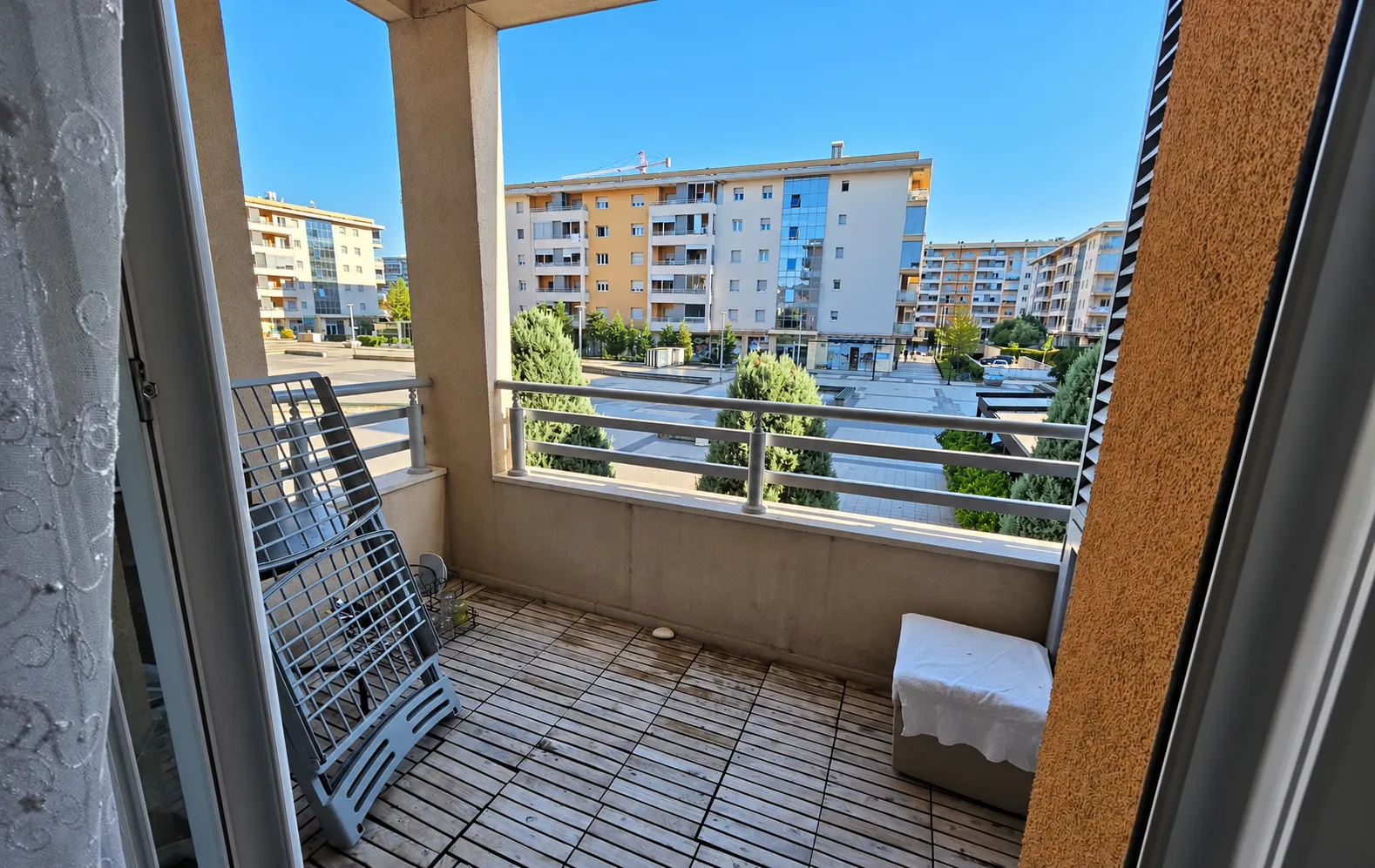 Natkriveni balkon sa drvenim podom i pogledom na naselje i zgrade.