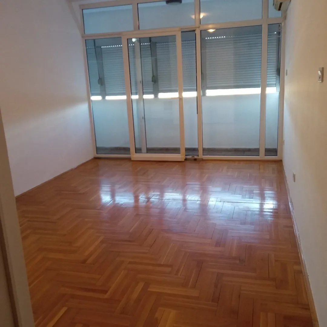 An empty room with polished parquet flooring and large glass doors.