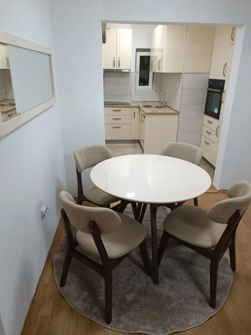 Dining area with a round table and four chairs, looking into the kitchen in the background.