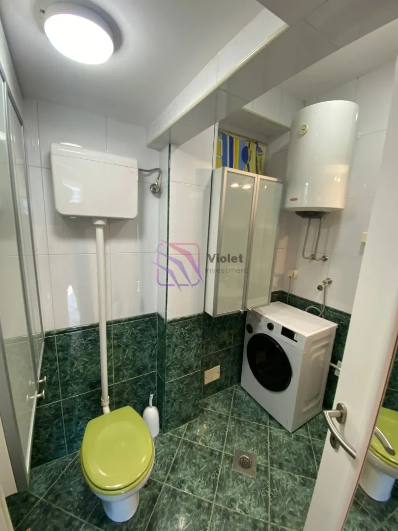 Manje kupatilo sa zelenim pločicama, wc šoljom, mašinom za veš i bojlerom.