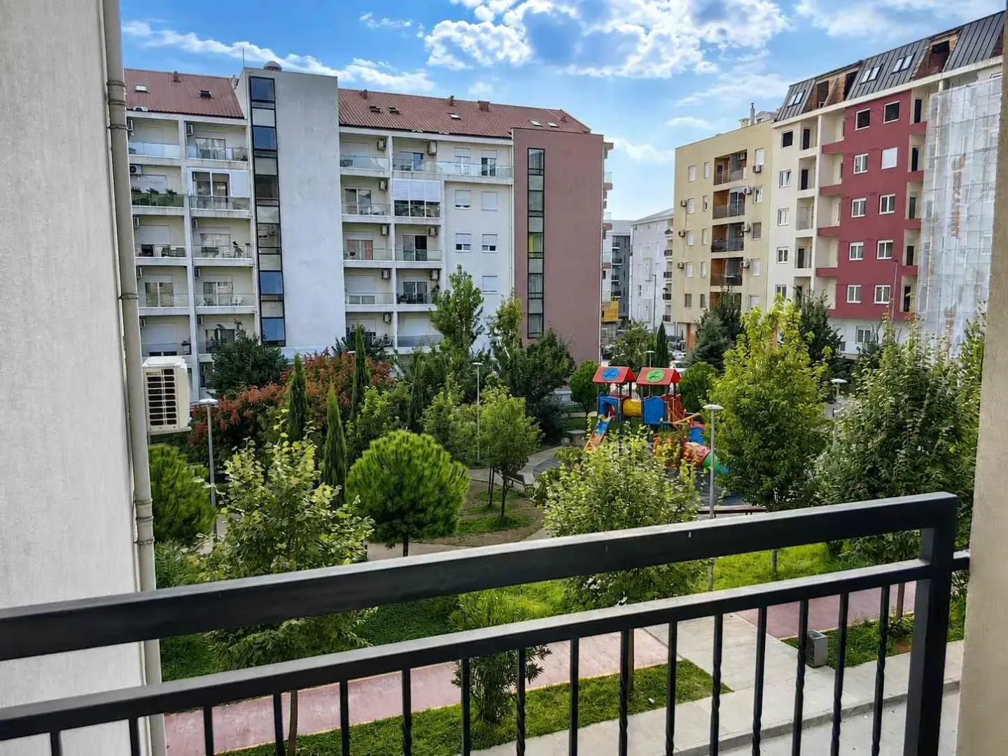 Pogled sa terase na okolne stambene zgrade i uređeno dvorište sa dječijim igralištem.