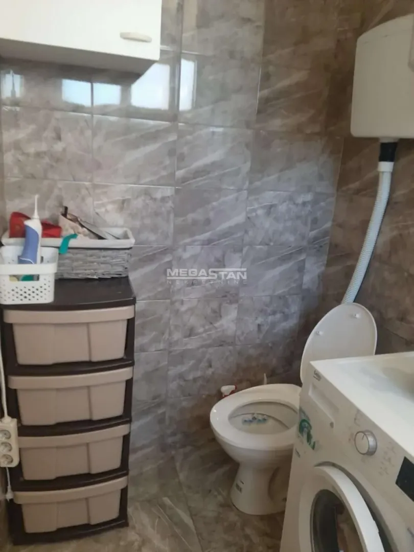 Manje kupatilo sa wc šoljom, mašinom za veš i zidnim pločicama.