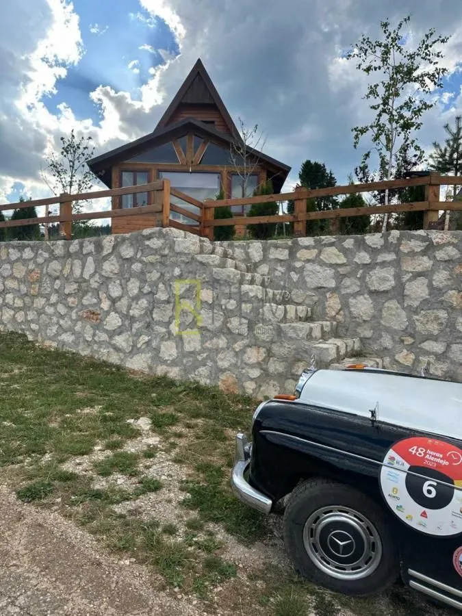 Drvena vikendica sa kamenim zidom i ogradom u dvorištu.
