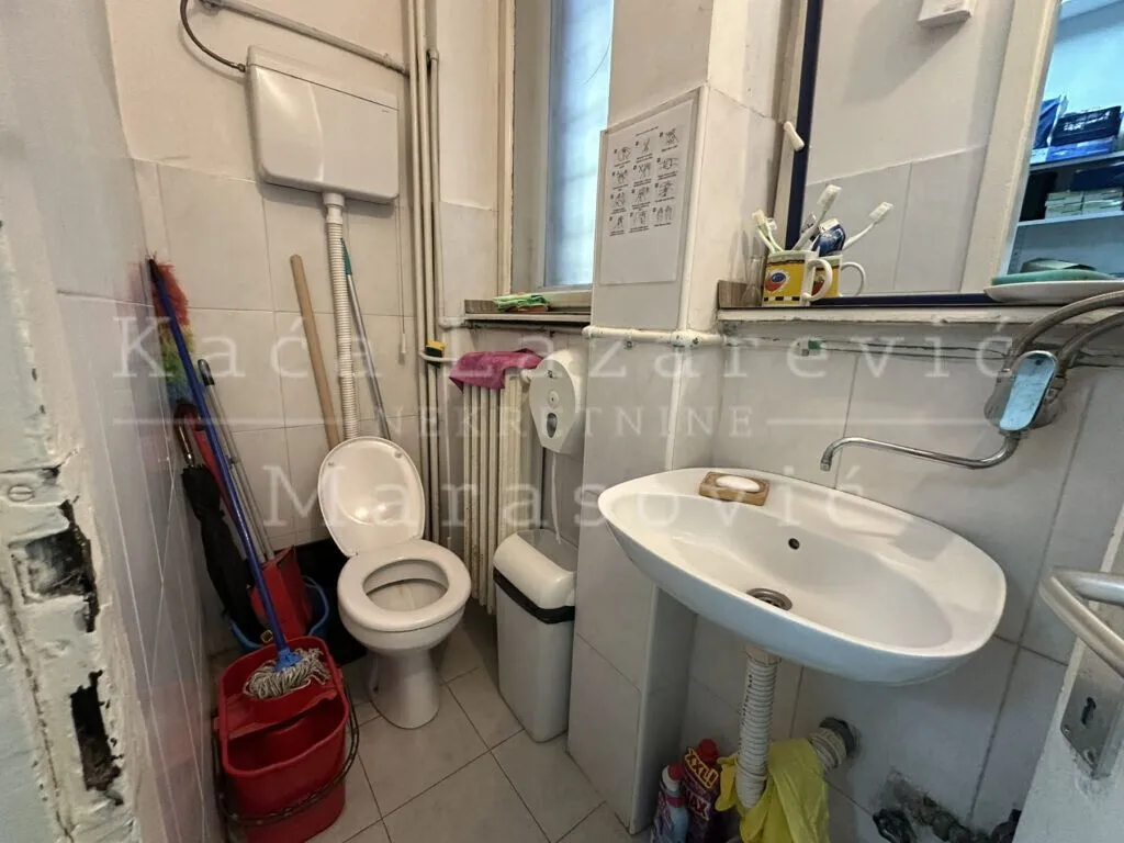 Small bathroom with a toilet, washbasin, and cleaning supplies.
