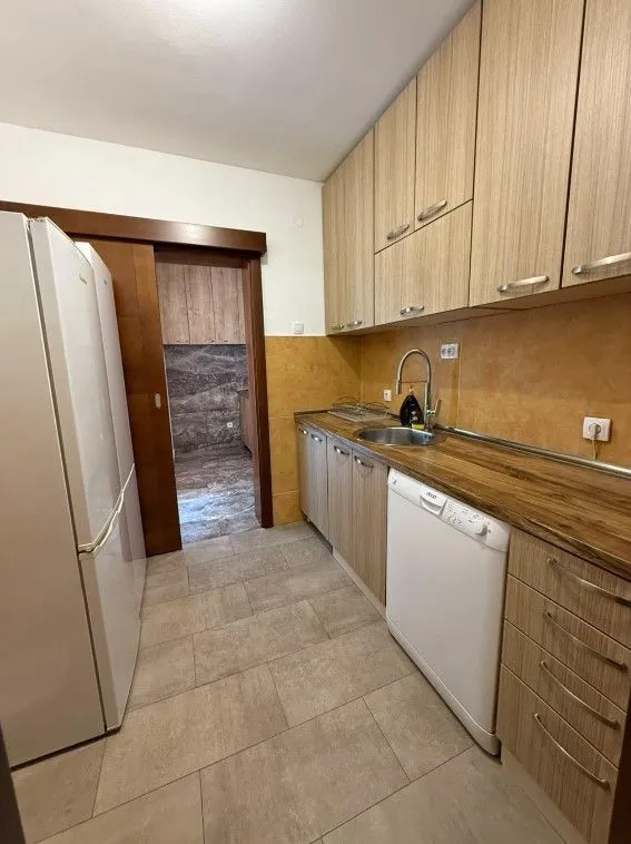 Manja kuhinja sa drvenim elementima, frižiderom i mašinom za sudove.