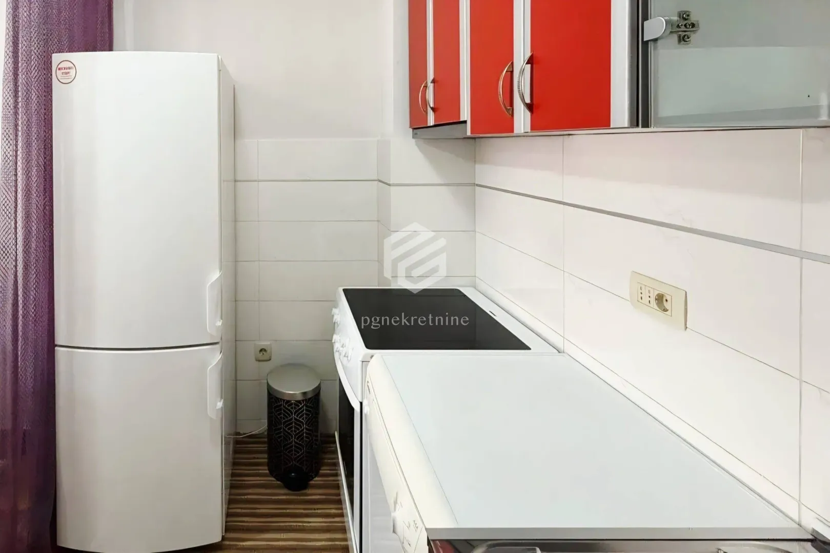 Small kitchen with a white refrigerator, stove and red cabinets.