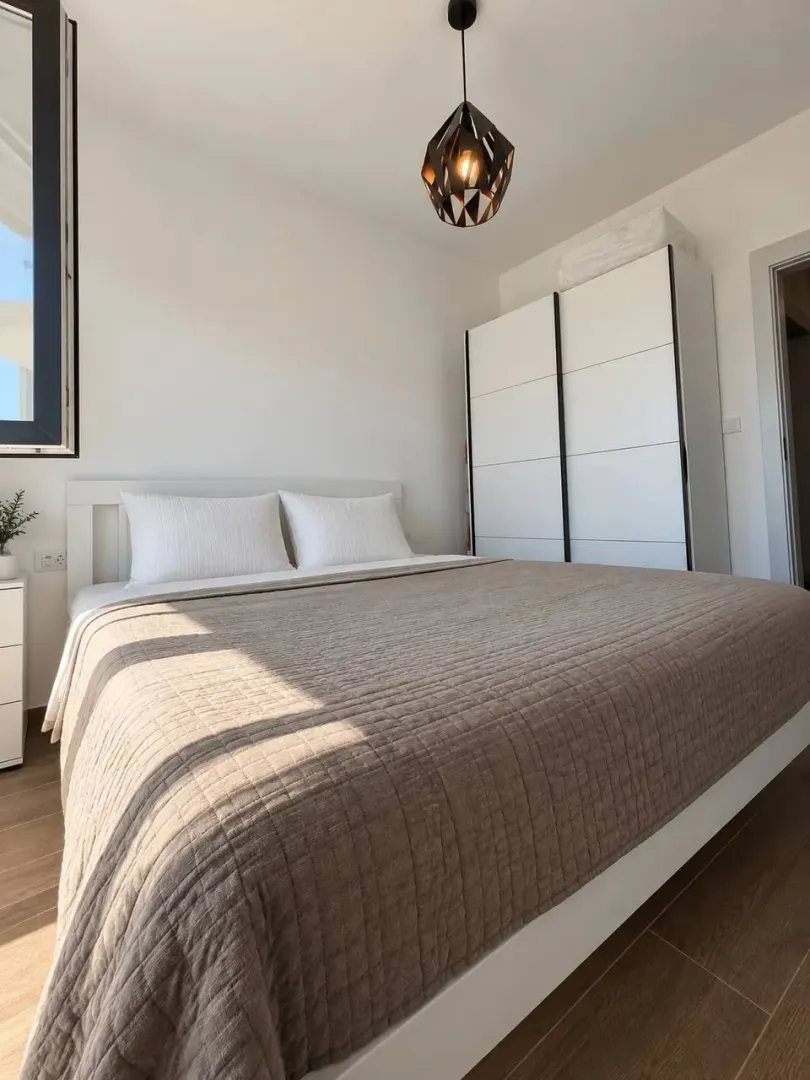 Svjetla i uredna spavaća soba sa bračnim krevetom, bijelim garderoberom i modernim lusterom.