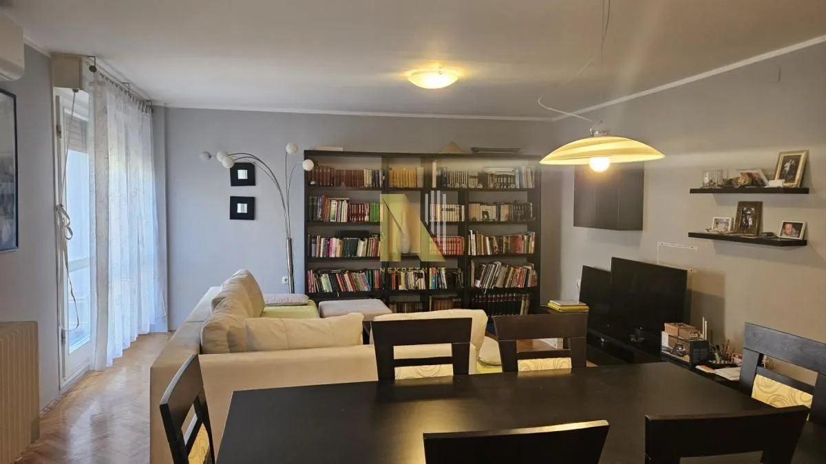 Dnevna soba sa garniturom, velikom bibliotekom i trpezarijskim stolom.