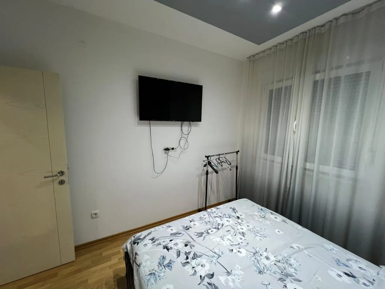 Small bedroom with a bed, wall-mounted TV, and window with curtains.