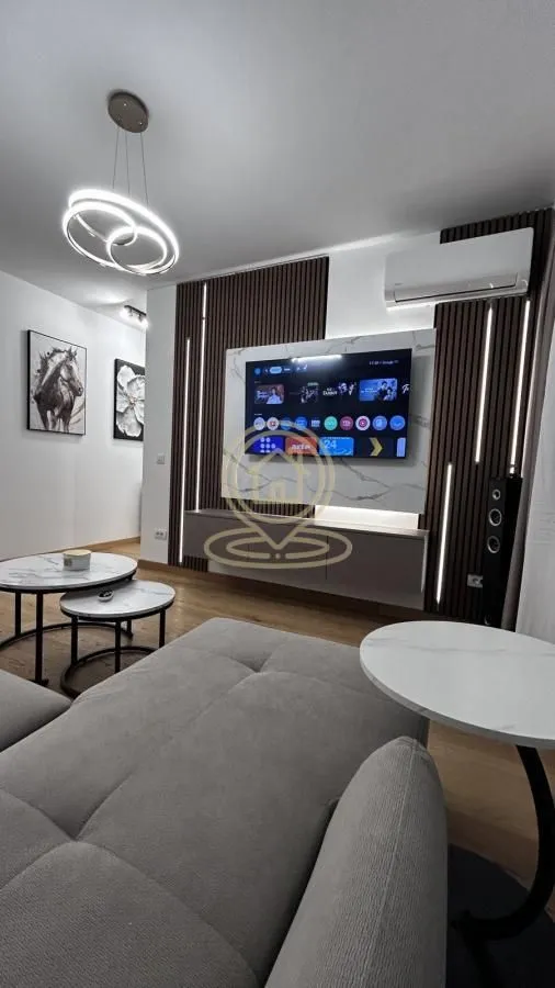 Living room with a corner sofa, wall-mounted TV, and modern lighting.