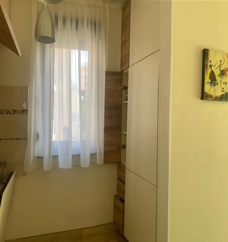 Part of the kitchen with white cabinets, a window with a curtain, and a pendant lamp.