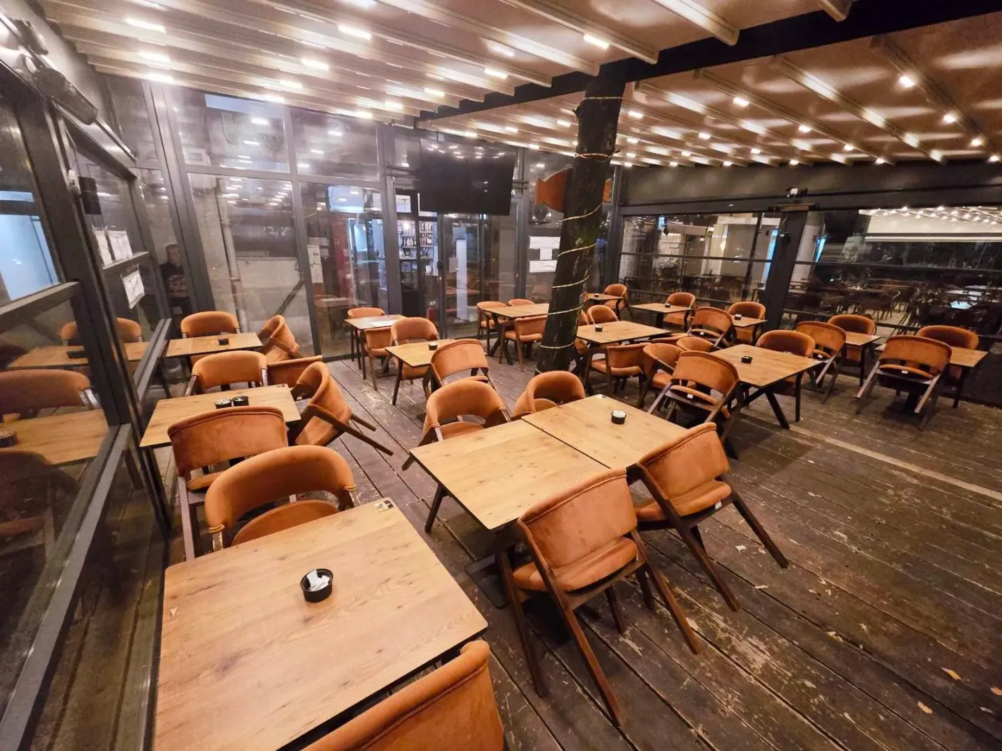 Covered restaurant terrace with wooden tables and orange chairs.
