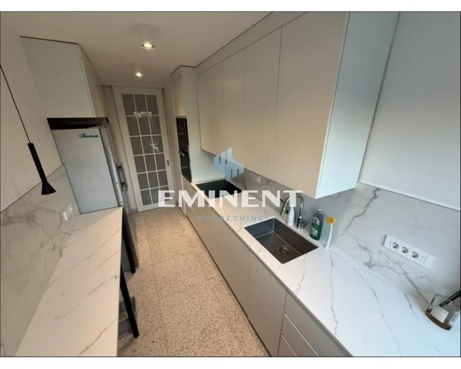 Long modern kitchen with white cabinetry and marble-textured countertops.