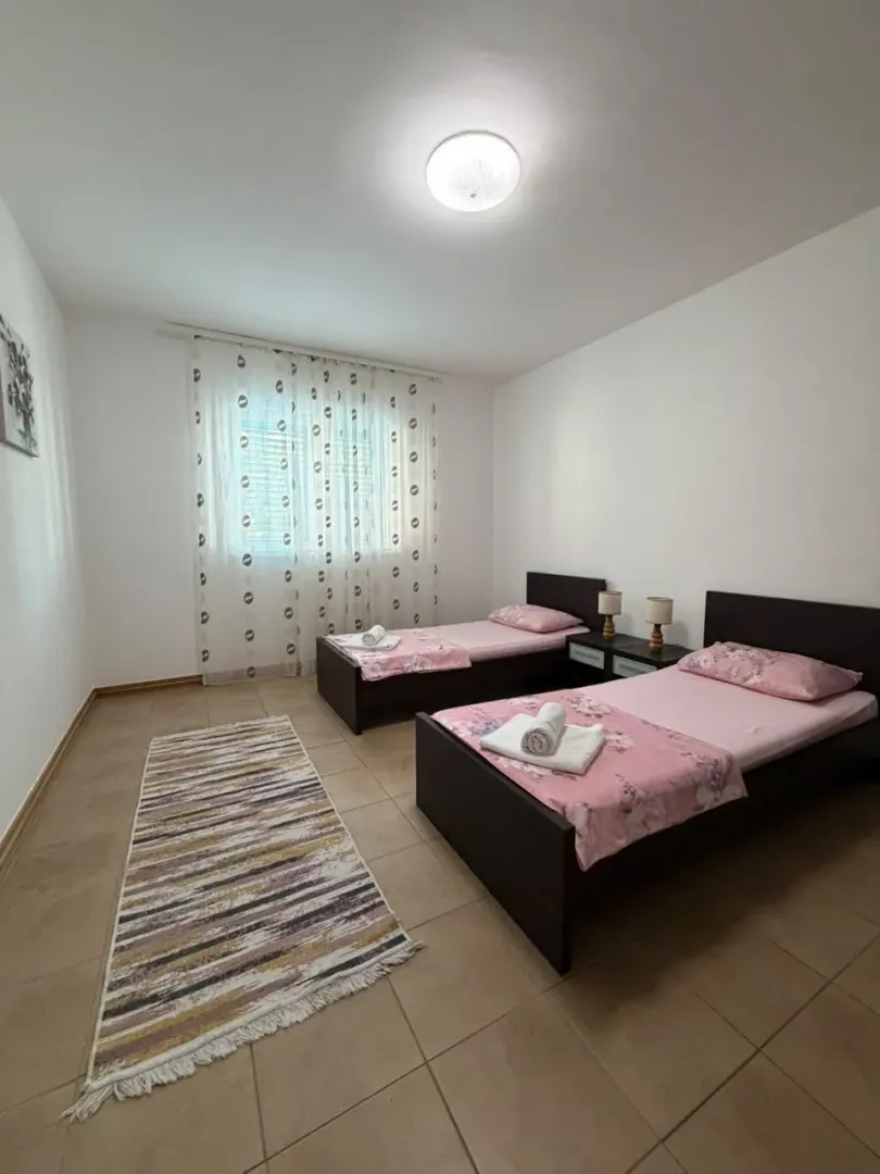 Spavaća soba sa dva singl kreveta i prozorom sa bijelim zavjesama.