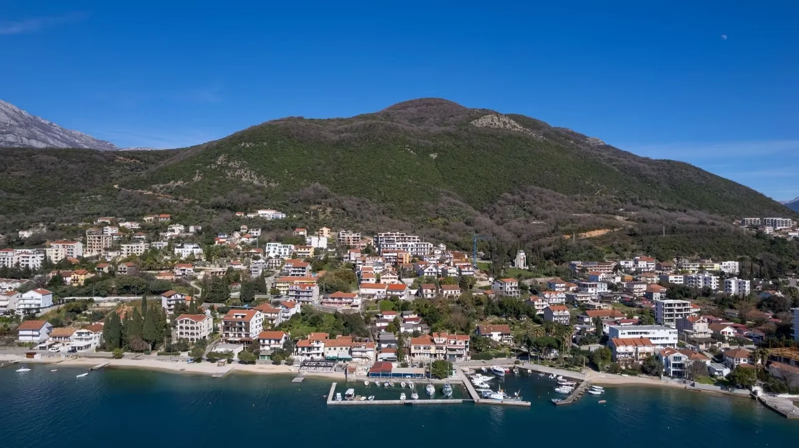 Pogled iz vazduha na obalu i primorsko naselje sa brdom u pozadini.