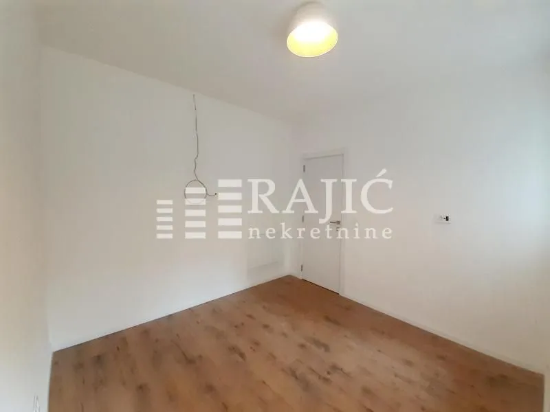 Empty room with white walls, wooden flooring, and a door.