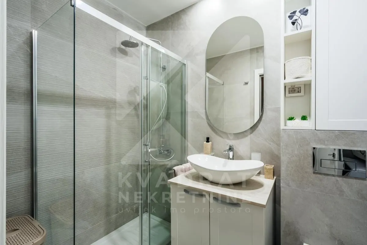 Modern bathroom with a walk-in shower, washbasin, and mirror.