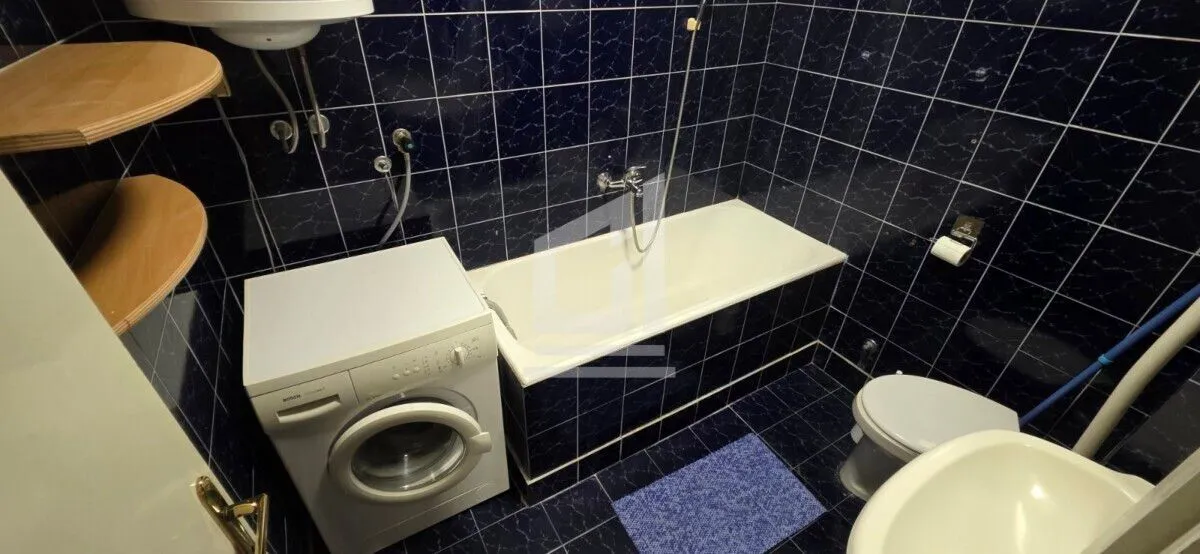 Kupatilo obloženo tamnoplavim pločicama sa kadom, veš mašinom i toaletom.